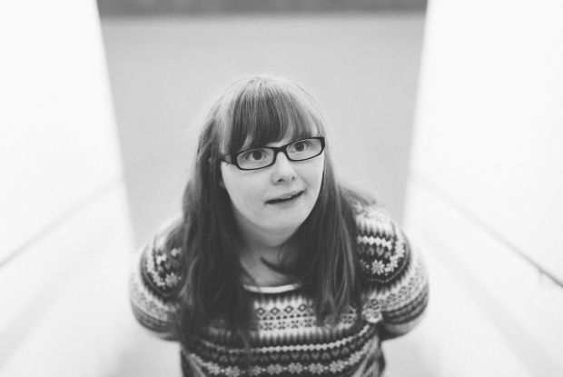 Ein schwarz-weiß-Foto einer jungen Frau mit Down-Syndrom. Sie hat lange Haare und trägt einen gestreiften Pullover.