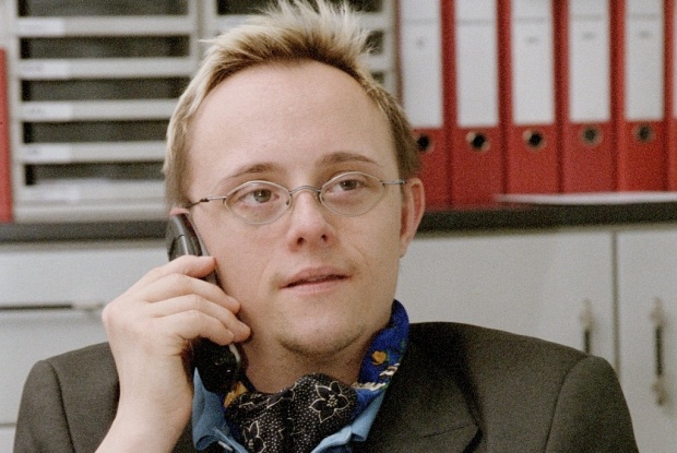 Ein Mann mit Down-Syndrom sitzt in einem Büro und telefoniert am Handy.