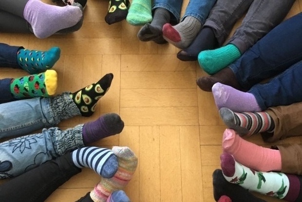 Eine Gruppe von Menschen sitzt im Kreis und streckt ihre Füße in die Mitte. Alle tragen bunte, verschiedene Socken.