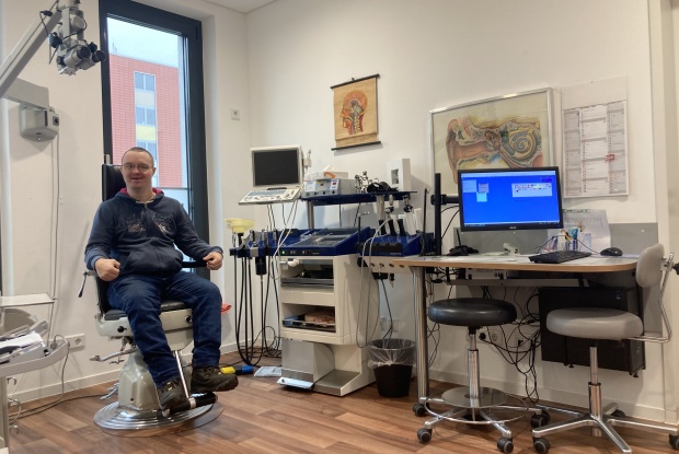 Ein Mann mit Down-Syndrom sitzt, vor vielen medizinischen Geräten, in einer Arztpraxis.