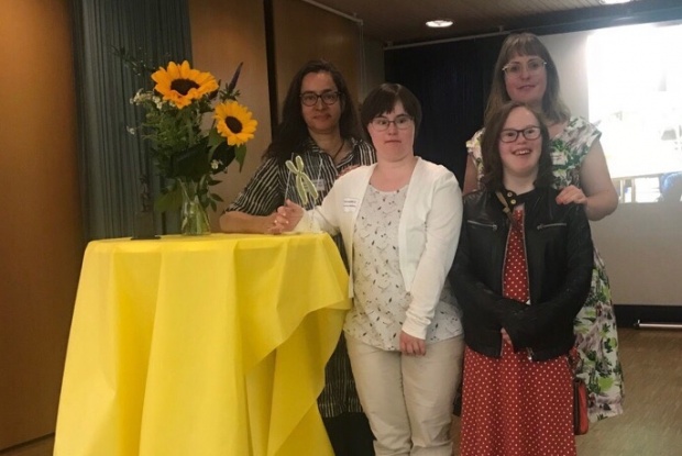 Das TOUCHDOWN 21 Team mit dem goldenen Chromosom, daneben ein Stehtisch mit Tischdecke und einem Blumenstrauß mit Sonnenblumen