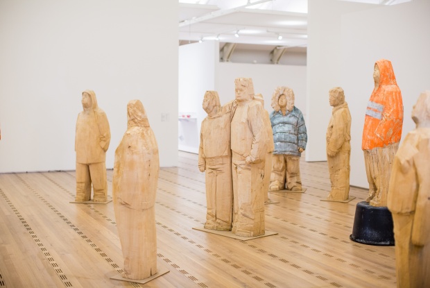 Mehrere lebensgroße, mit der Kettensäge hergestellte Holzfiguren in einem hellen Museumsraum. Zwei von ihnen sind farbig, die anderen aus hellem Holz.