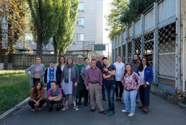 Eine Gruppe von etwa 20 Personen mit und ohne Down-Syndrom steht vor einem langgestreckten, flachen Gebäude, im Hintergrund ist ein Schild mit dem Schriftzug iZone zu sehen.