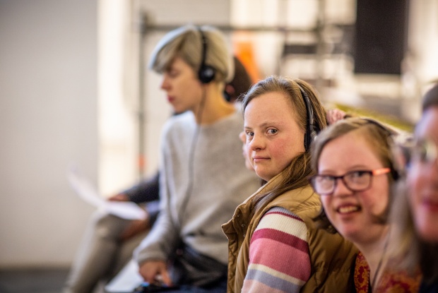 3 Frauen, 2 davon mit Down-Syndrom, sitzen in einer Reihe nebeneinander. Sie hören die Übersetzung über Kopfhörer.