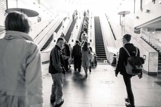 Ein Mann mit Down-Syndrom im Ausgangsbereich der U-Bahn. Vor ihm sieht man mehrere Rolltreppen, um ihn herum sind Passanten und Passantinnen unterwegs.