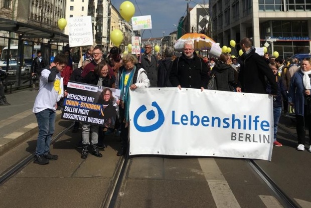 Menschen mit und ohne Down-Syndrom laufen mit Transparenten durch Berlin.