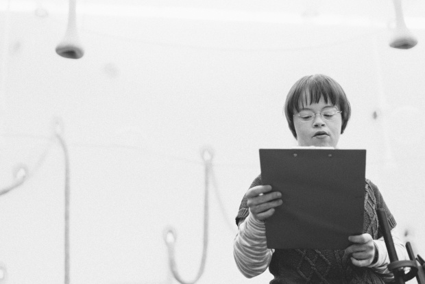 Eine Frau mit Down-Syndrom hält eine Klemmmappe in der Hand und liest einen Text vor.
