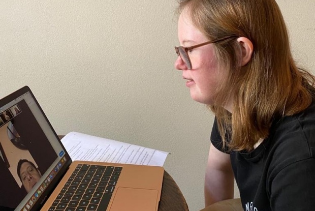 Eine junge Frau mit Down-Syndrom sitzt vor einem aufgeklappten Laptop mit einem Videotelefonat.