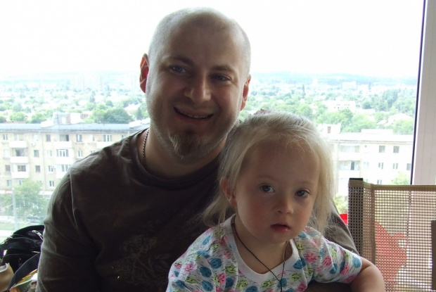 Ein Vater hat seine blonde Tochter mit Down-Syndrom auf dem Schoß.